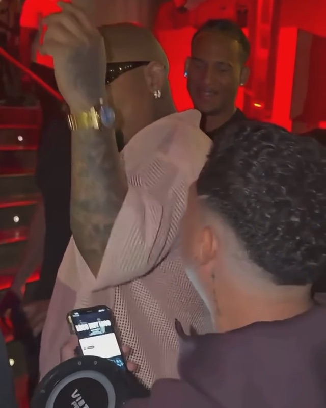 Dame Hombro AI clip: the freestyler throws one arm up as the crowd behind him smiles